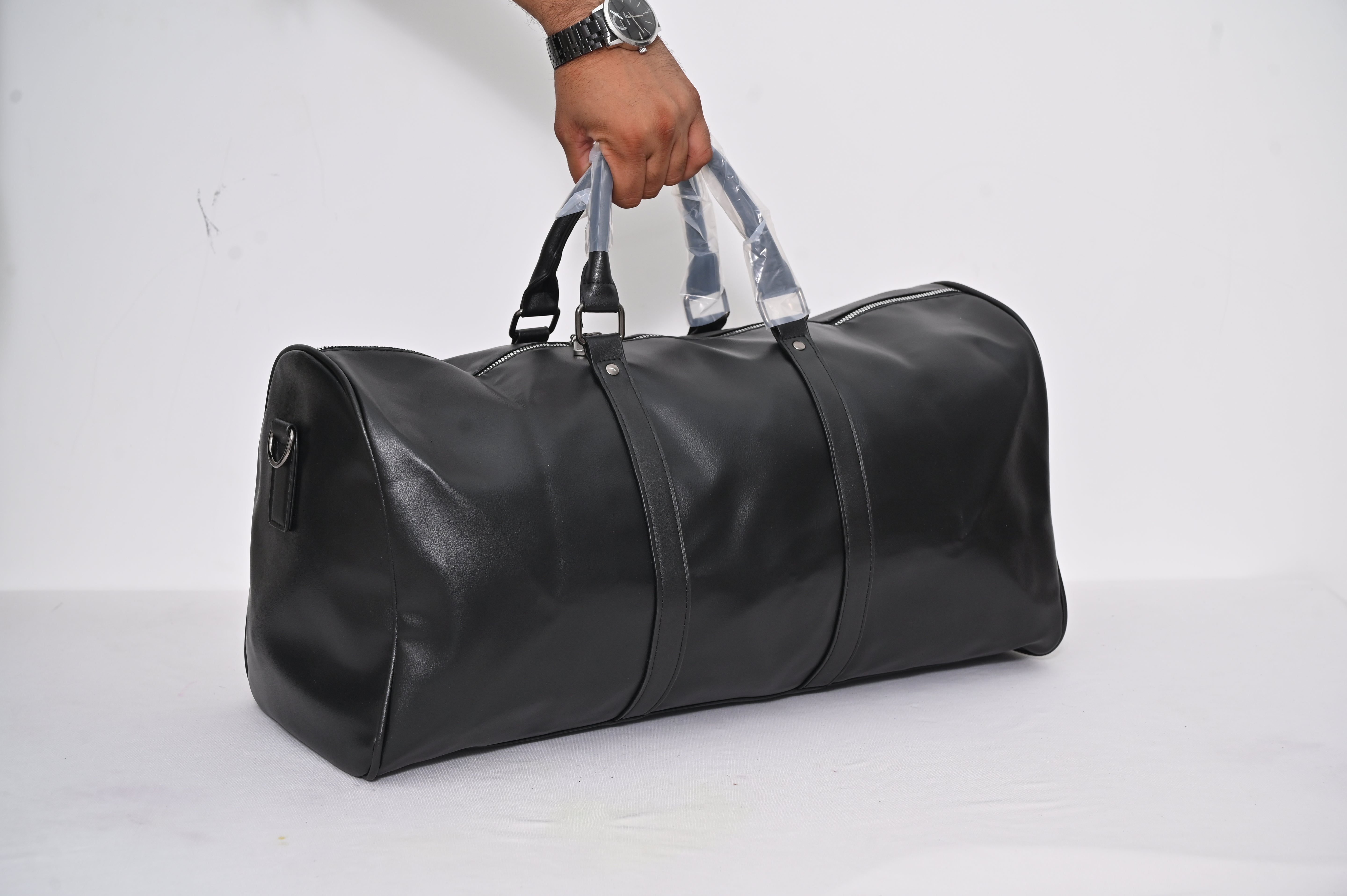 Black duffel bag held by a hand on a white background